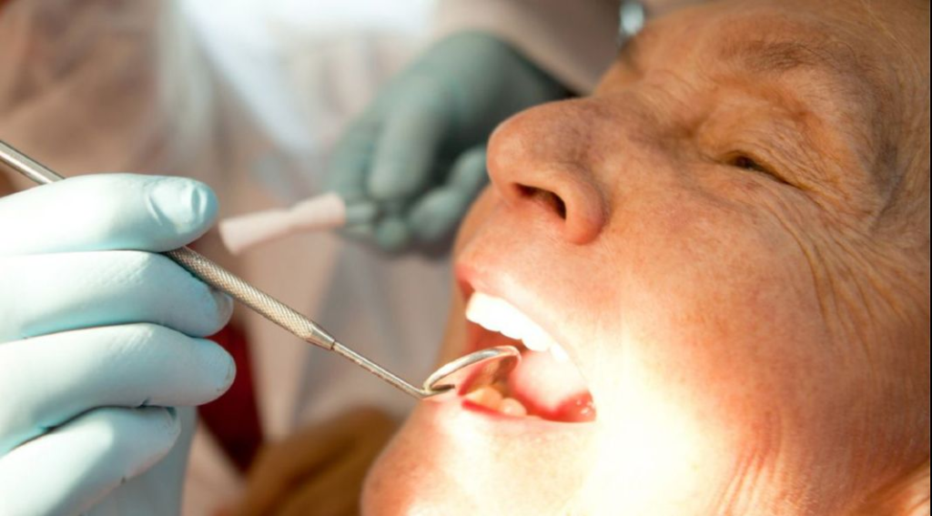 Senior woman receiving a dental exam from a dentist, with a mirror being used to check her teeth