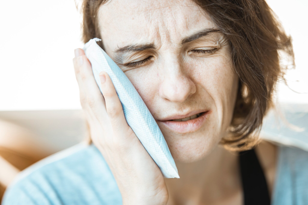 Woman holding ice pack to cheek, experiencing dental pain and needing emergency dental care